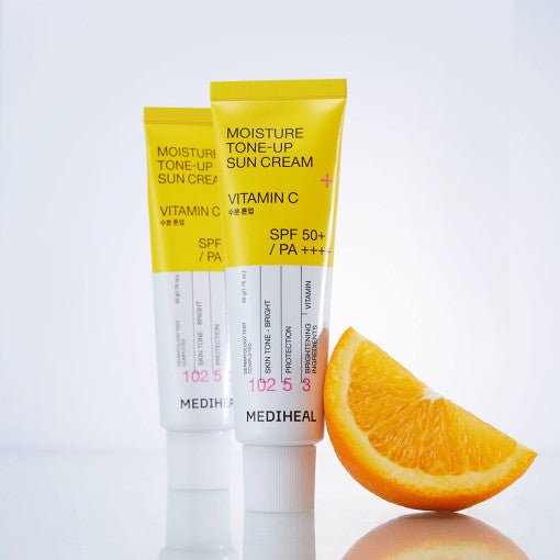 Two yellow and white sunscreen tubes with SPF 50+ and a fresh orange slice on a reflective surface