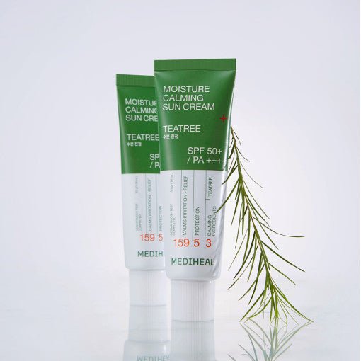 Two green and white tubes of moisture calming sun cream with tea tree beside a thin green branch on white surface