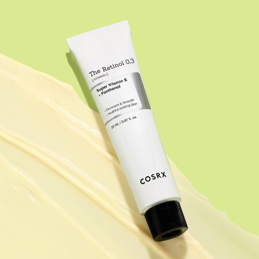 White tube of retinol cream with vitamin E and panthenol on pale yellow cream smear and light green background