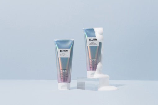 Two iridescent tubes of gentle cleansing foam on pale blue surface, one with white foam flowing over clear block