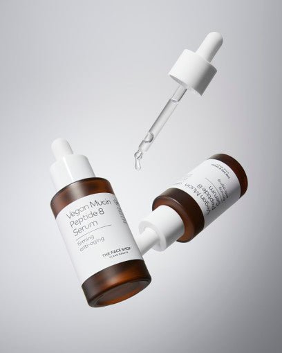 Two brown glass serum bottles with white labels and droppers, one with serum drop falling from pipette