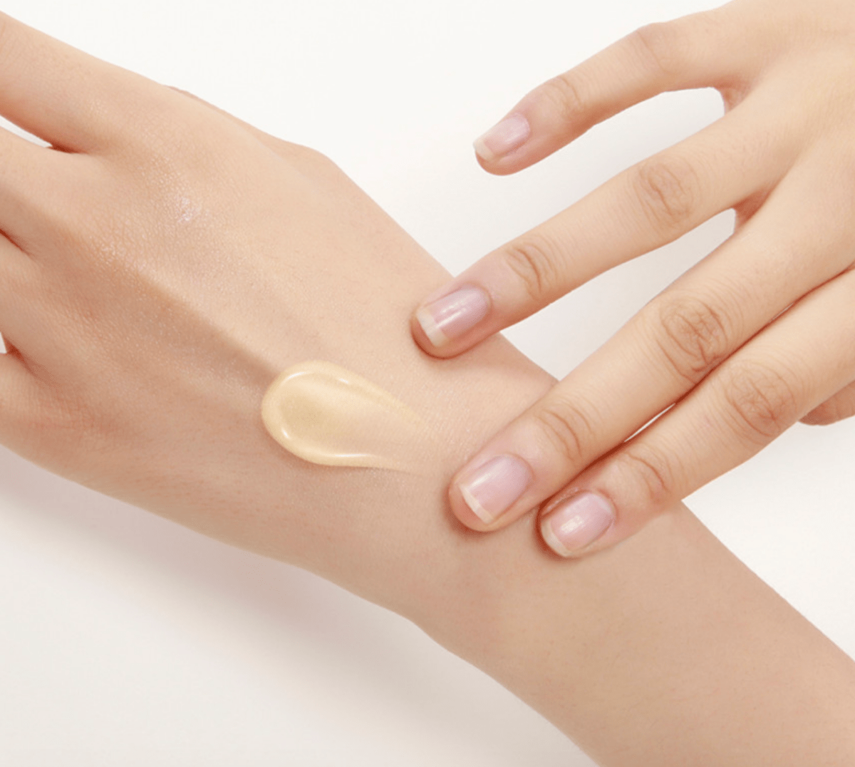 Creamy pale lotion being gently spread on the back of a hand to show soft, moisturized skin effect