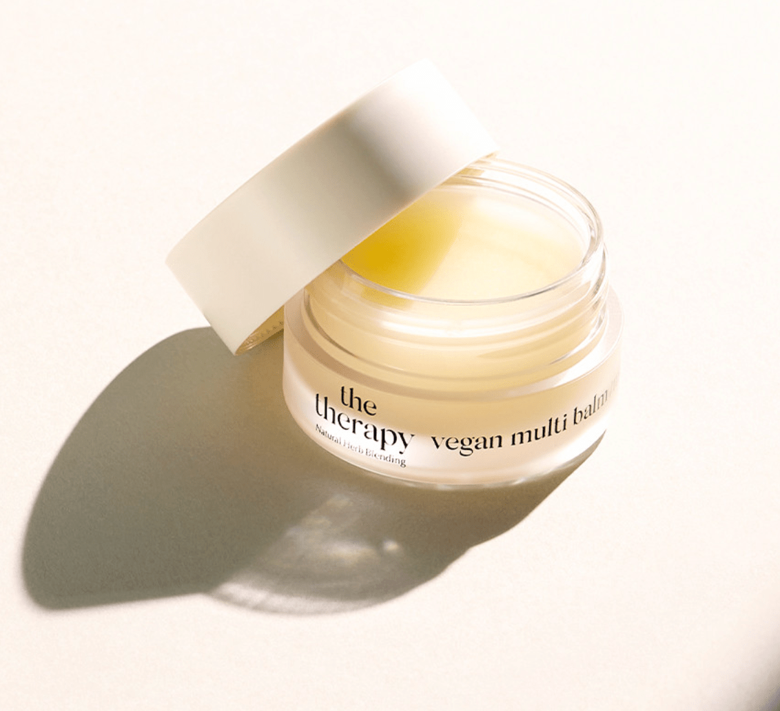 Open jar of moisturizing vegan multi balm with pale yellow balm inside on a light background with soft shadow