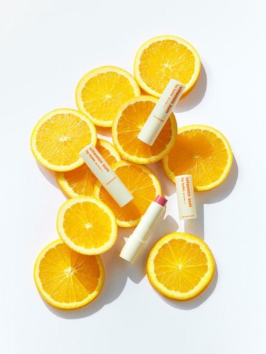 Lip balm tubes with bright orange text placed on and around fresh orange slices on white background