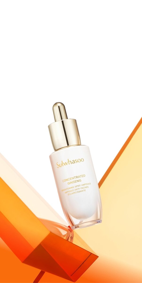 White and gold dropper bottle of ginseng brightening ampoule balanced on translucent orange geometric shapes against white background