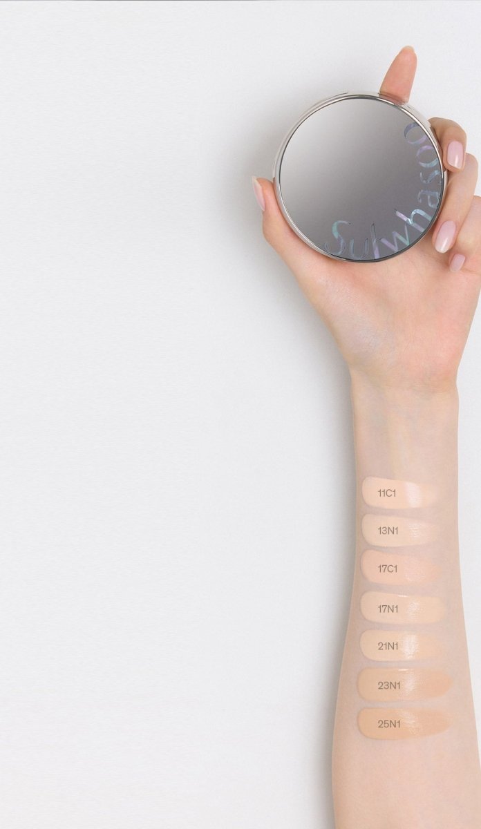 Hand holding sleek silver compact with cushion foundation swatches labeled in natural shades on inner forearm