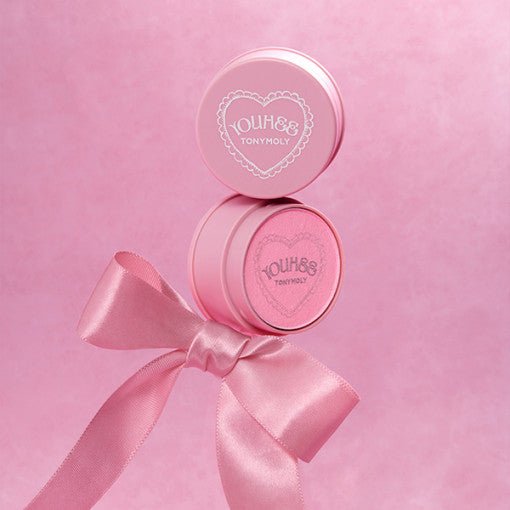 Round pink container of hydrating jelly blusher with heart logo and satin ribbon on soft pink backdrop