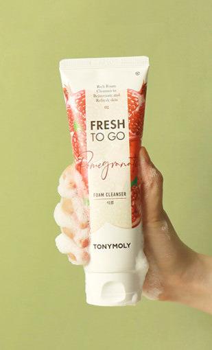 Hand holding pomegranate-scented foam cleanser tube with white foam on fingers against light green background