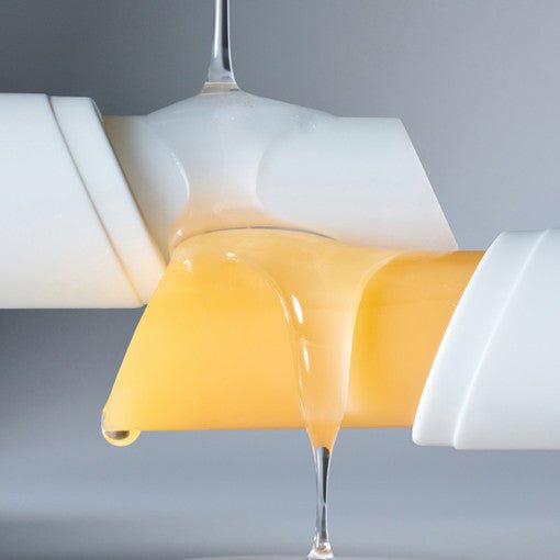 Close-up of yellow balm with honey-like liquid dripping from the tube against a light gray background