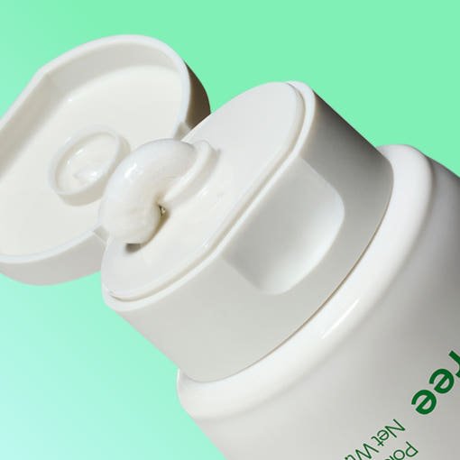 Close-up of white cleansing foam gently dispensed from white flip-top tube against light green background