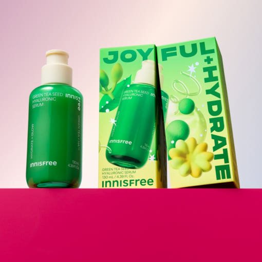 Green bottle of hydrating serum with green tea seed extract beside vibrant green and yellow product packaging on pink surface