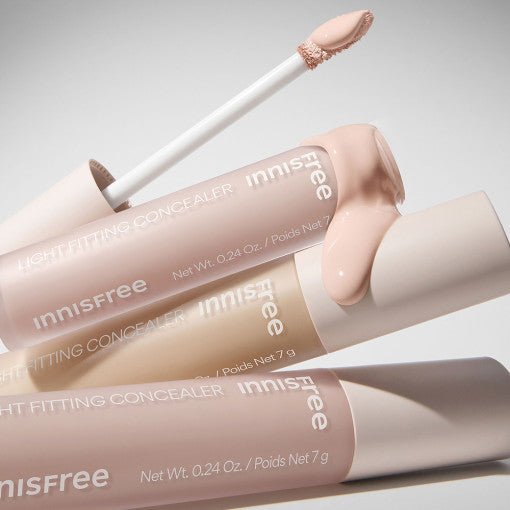 Three tubes of light fitting concealer in soft neutral shades with one applicator showing creamy texture spill