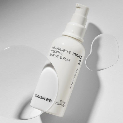 White pump bottle of nourishing hair oil serum with smooth translucent drops on light background