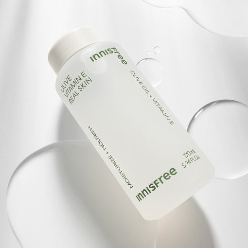 Frosted bottle of moisturizing skin toner with olive oil and vitamin E ingredients on white surface with liquid drops
