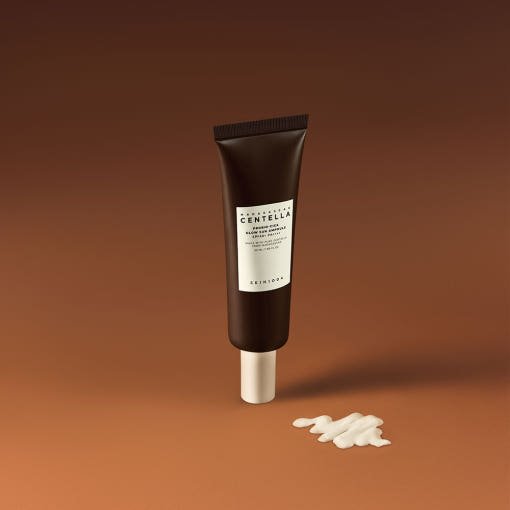Dark brown tube of glow sun ampoule with white cap and creamy product swatch on warm brown background for UV protection