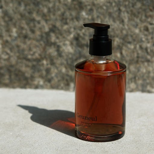 Transparent amber bottle with black pump dispensing moisture-boost body wash on textured stone surface background