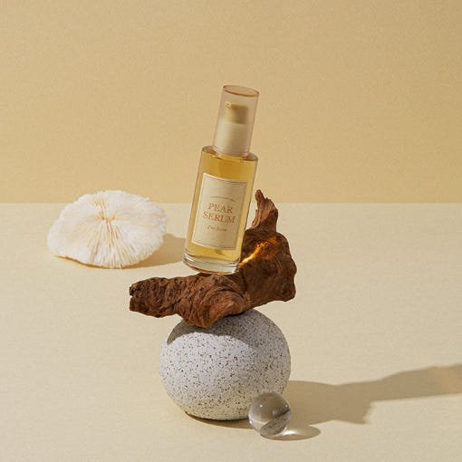 Glass bottle of hydrating pear serum on balanced natural elements with soft beige background
