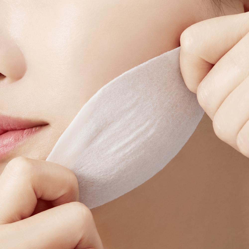 Close-up of a person gently applying a soft white toner pad to smooth cheek for hydration boost effect