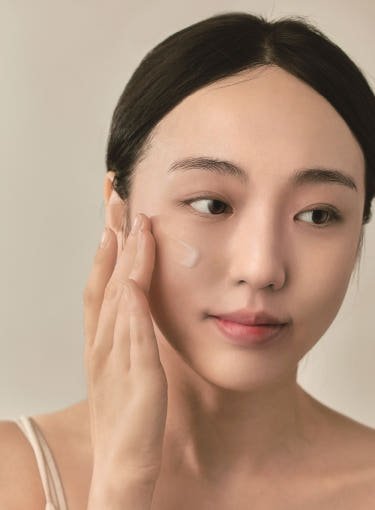 Woman with clear skin gently applying lightweight serum to her cheek in natural light setting