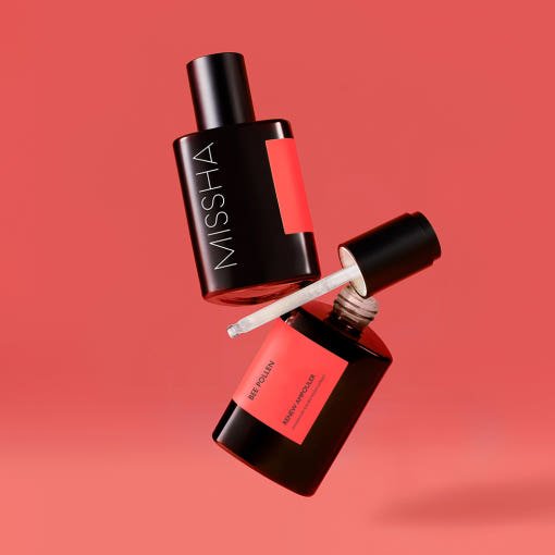 Two black ampoule bottles with coral labels floating on coral background highlighting skin energy benefits