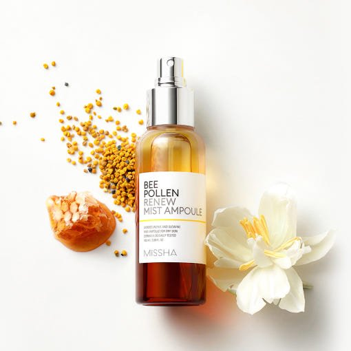 Amber-colored spray bottle of bee pollen mist ampoule surrounded by bee pollen granules and a white flower on white background