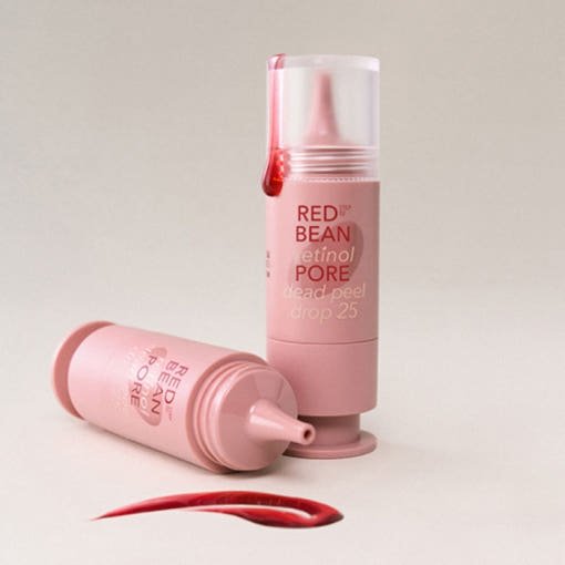 Two pink exfoliating serum tubes with red liquid drop and smear on a light beige surface