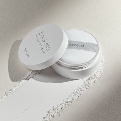 Open white jar of translucent finishing powder with soft puff and powder streak on light surface