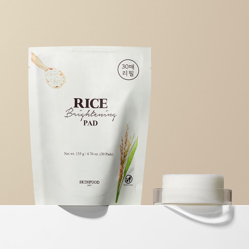 White refill pack of brightening rice skincare pads beside closed transparent container on beige surface
