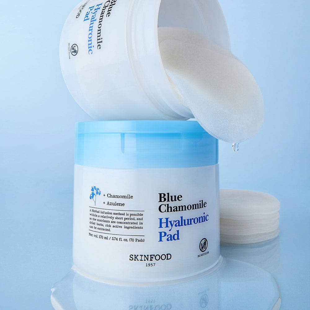 Open jar of blue chamomile hyaluronic pads with one pad dripping hydration over second container on blue background
