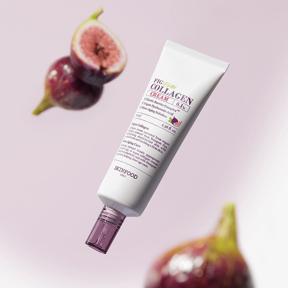 Tube of vegan collagen cream with purple cap surrounded by fresh figs on soft pink background