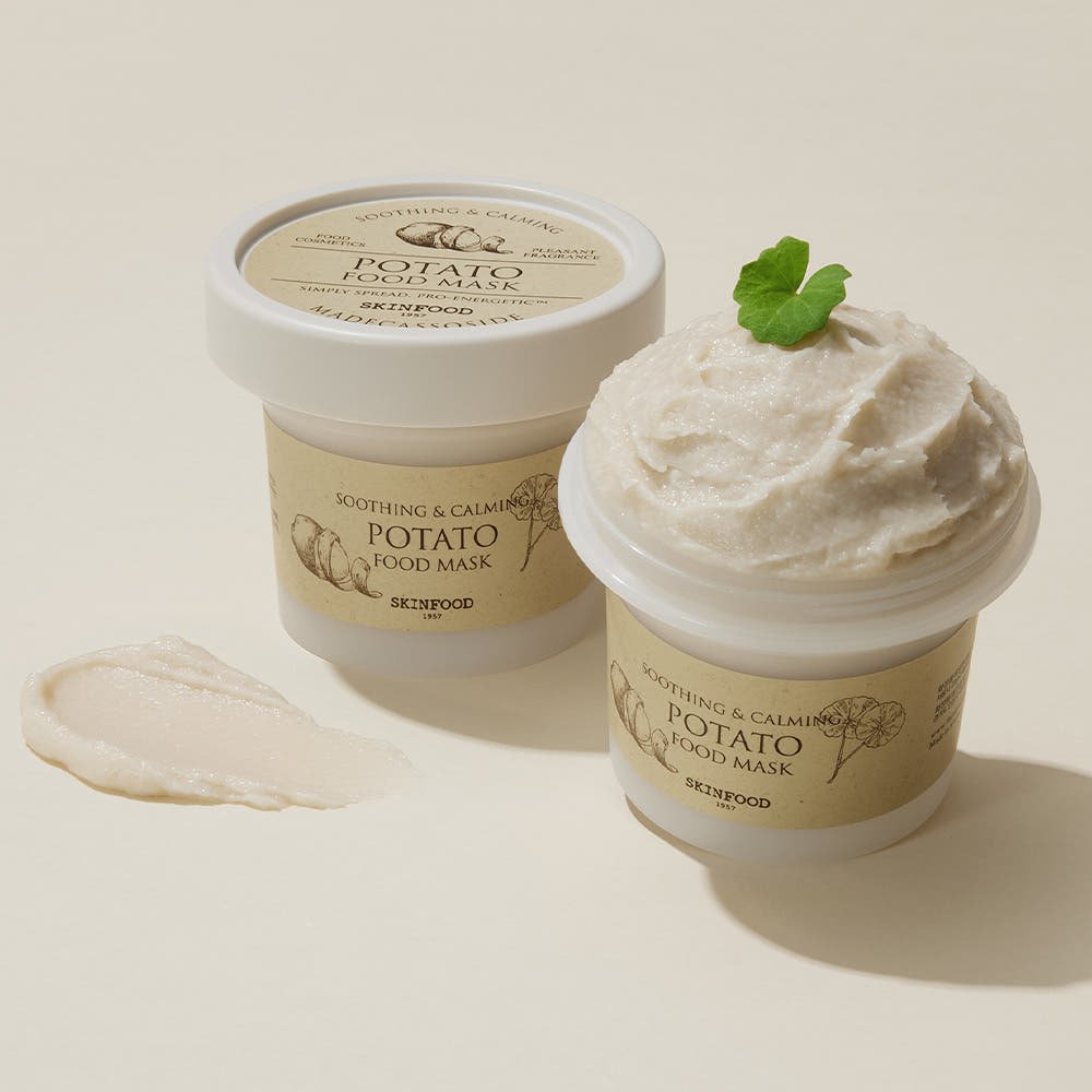 Open jar of creamy potato food mask with mint leaf garnish beside closed container and smooth product smear on beige surface
