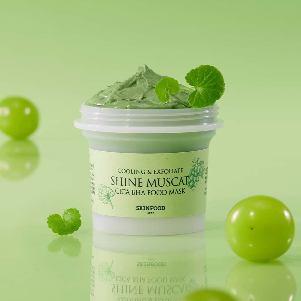 Open jar of cooling green food mask with creamy texture and fresh leaves on light green background for deep cleansing