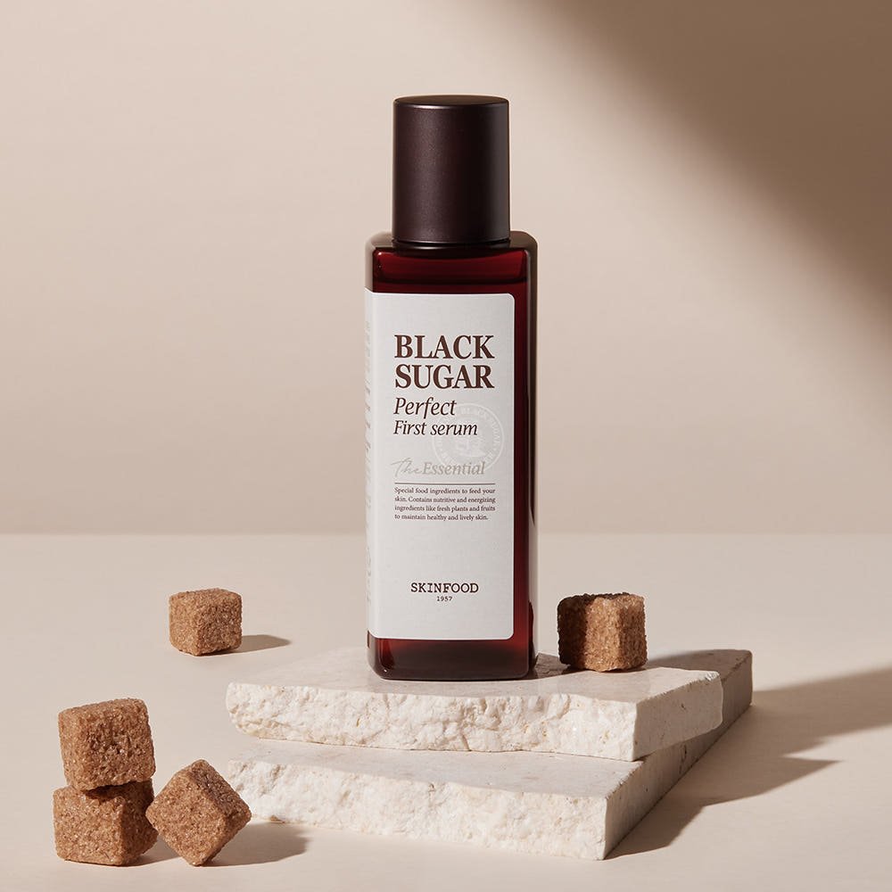 Dark amber bottle of hydrating Black Sugar serum standing on textured white stone with stacked sugar cubes around it