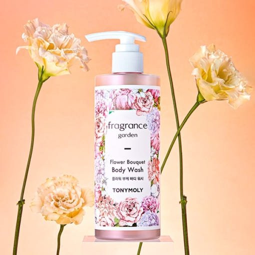 Pink floral body wash bottle with pump surrounded by soft peach flowers against a warm background