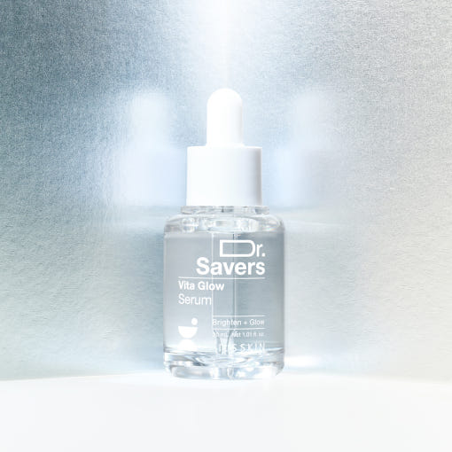 Clear glass dropper bottle of brightening serum with white cap on reflective silver background