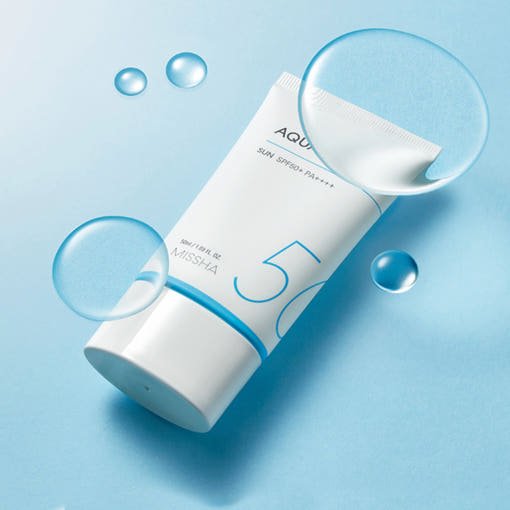 White tube of high protection aqua sunblock with SPF50+ PA++++ and water droplets on light blue surface