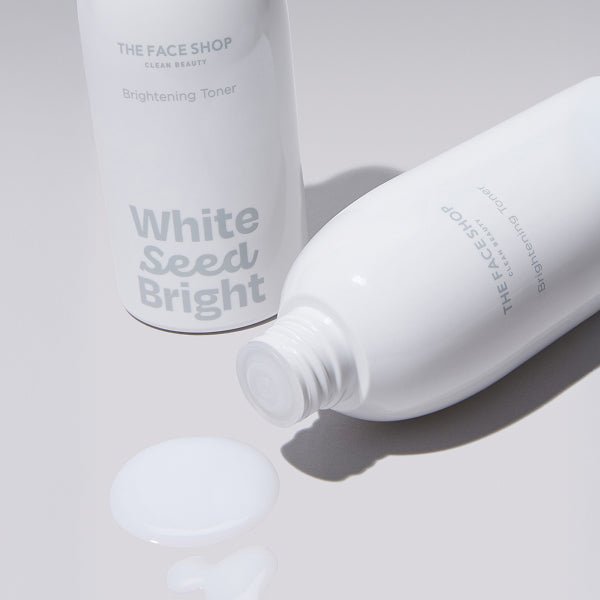 Two white bottles of brightening toner with spilled liquid on smooth light surface and soft shadows