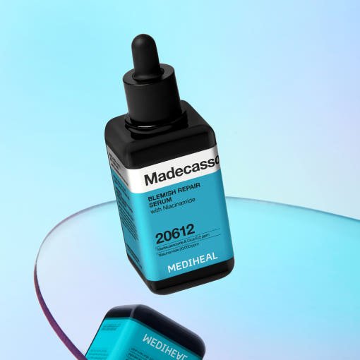 Black dropper bottle with blue label for blemish repair serum standing on reflective surface against light blue background