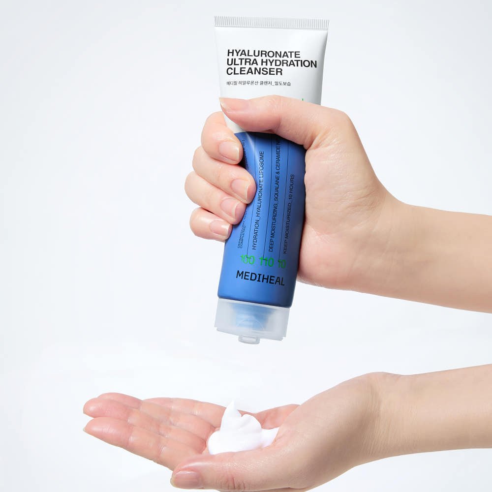 Hand dispensing creamy white cleanser from blue and white tube labeled hyaluronate ultra hydration cleanser
