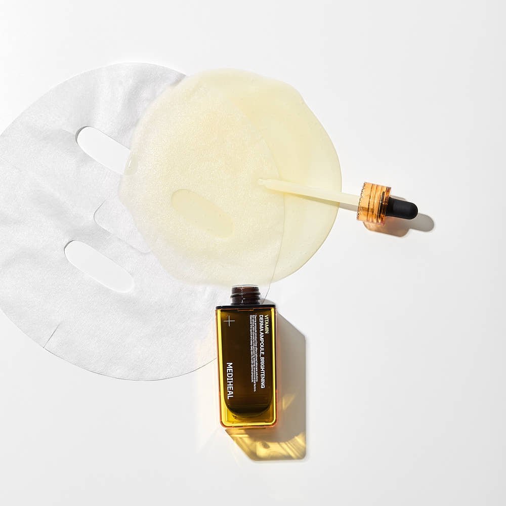 Amber serum bottle with dropper releasing liquid onto translucent sheet mask on white background