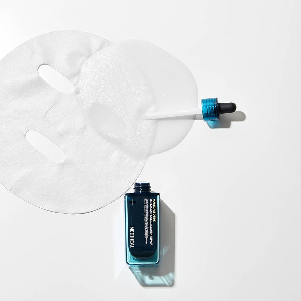 Open blue serum bottle with dropper and unfolded white sheet mask on white background