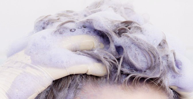 Person wearing a glove massaging purple shampoo foam into hair to nourish and cleanse strands