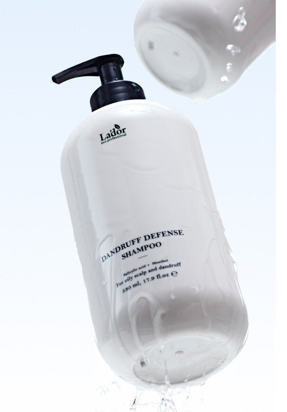 White shampoo bottle with black pump dispensing clear liquid against pale blue background