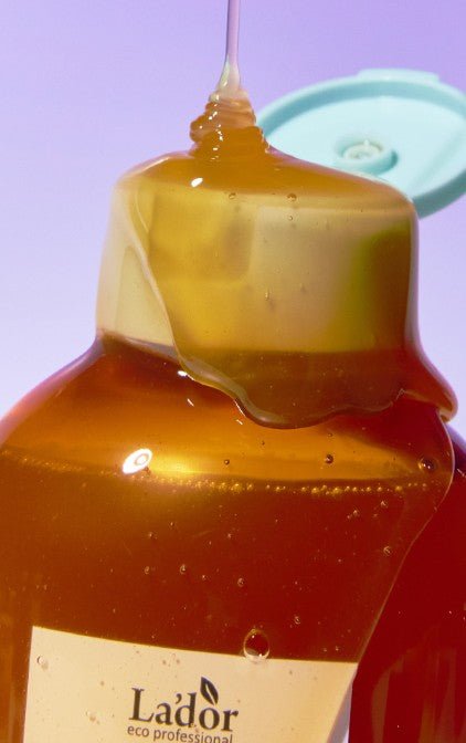Close-up of amber gel shampoo dripping from the opened cap of a bottle against a soft purple background