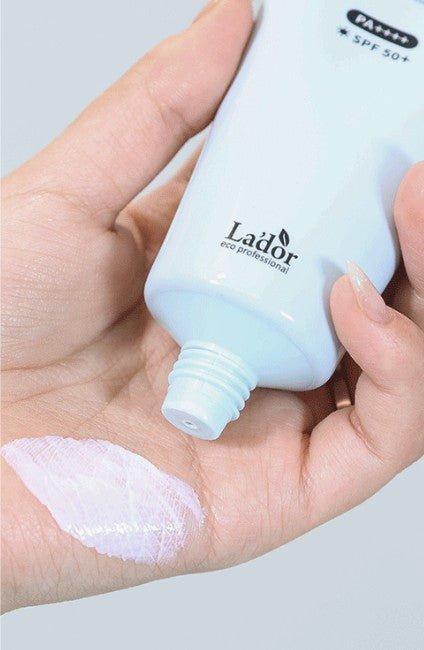 Hand holding white sunscreen tube with a small amount of light pink cream spread on palm showing texture and consistency