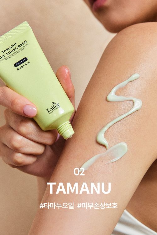 Hand holding light green sunscreen tube dispensing lotion on forearm with smooth, creamy texture visible.