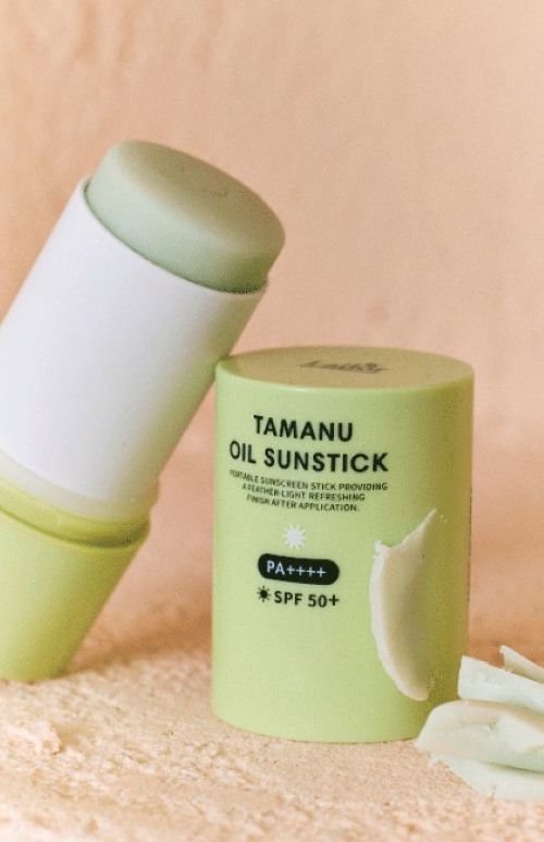 Green portable sun stick with SPF50+ and PA++++ protection shown with cap beside it on beige surface