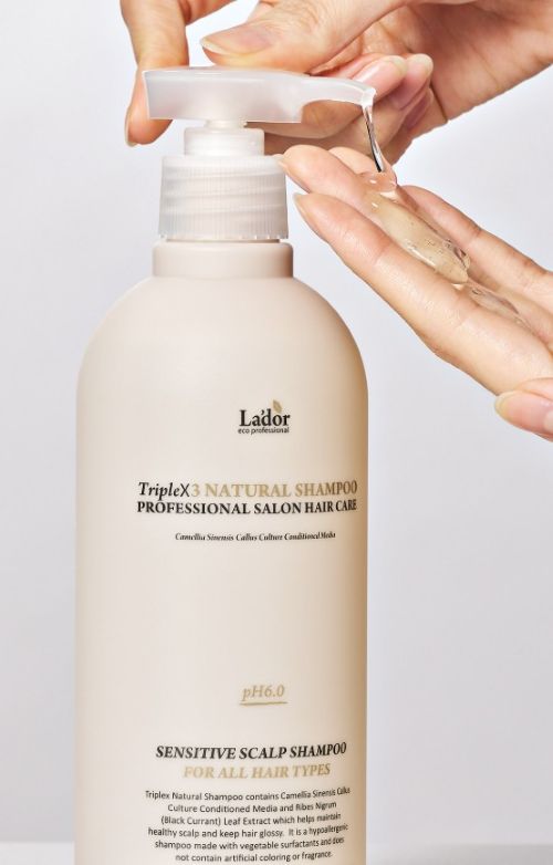 Hand dispensing clear gel shampoo from a beige pump bottle labeled for sensitive scalp and gentle cleansing