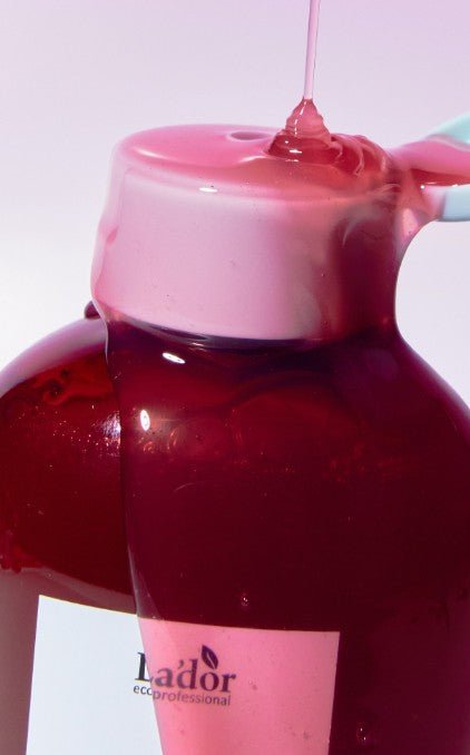 Close-up of translucent pink gel being poured over a shampoo bottle cap labeled Lador for effective cleansing.