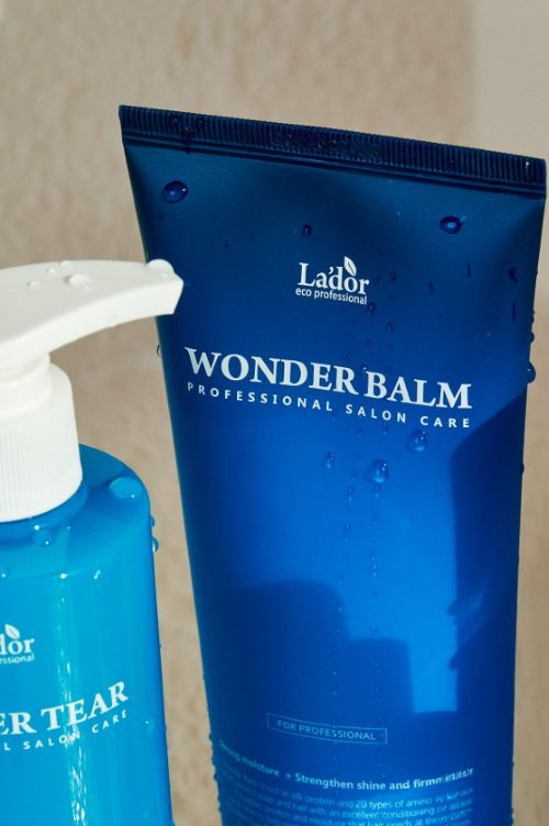 Blue tube of nourishing balm with water droplets on the surface against beige background